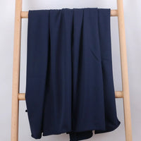 Un morceau de Tissu French Terry en coton extensible de Longan Craft France est drapé sur un porte-échelle en bois clair sur un fond blanc uni, mettant en valeur ce tissu confortable et multicolore idéal pour les vêtements de sport.