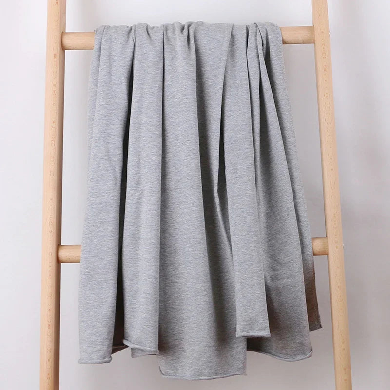 Le Tissu French Terry en coton extensible au mètre de Longan Craft France, un tricot confortable idéal pour les vêtements de sport, est drapé en plis amples sur deux barreaux d'une échelle en bois clair sur un fond blanc uni.