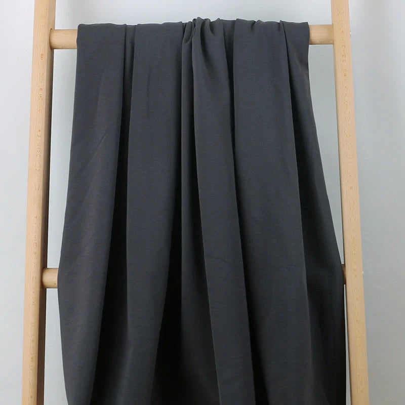 Un tissu multicolore et confortable en coton extensible French Terry de Longan Craft France est drapé sur une échelle en bois clair sur un fond blanc uni - idéal pour les vêtements de sport et vendu au mètre.