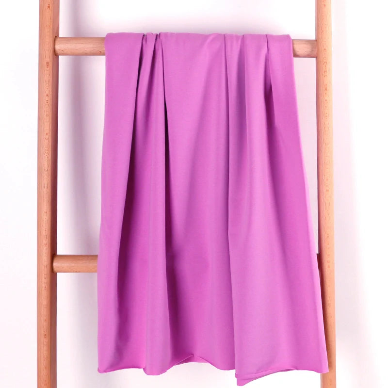 Un pli en tissu éponge rose en coton extensible de Longan Craft France est drapé sur le barreau central d'une échelle en bois clair, sur un fond blanc uni.