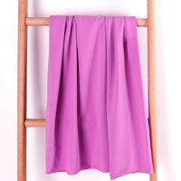 Un pli en tissu éponge rose en coton extensible de Longan Craft France est drapé sur le barreau central d'une échelle en bois clair, sur un fond blanc uni.