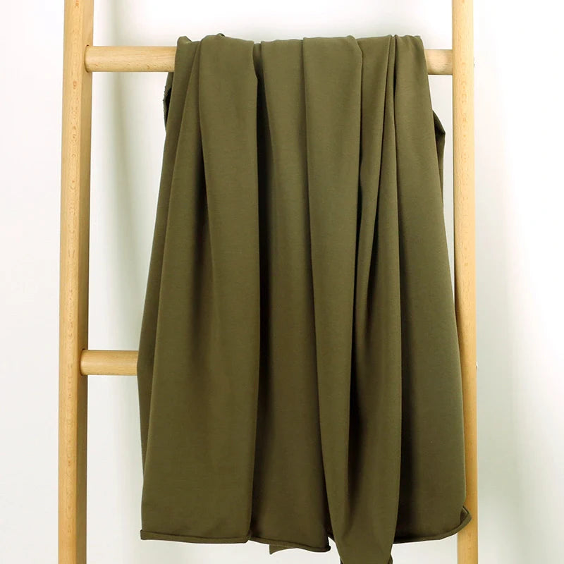 Le Tissu French Terry en coton extensible au mètre de Longan Craft France, présenté drapé sur une échelle en bois clair sur fond blanc, est un tricot multicolore confortable idéal pour les vêtements de sport.