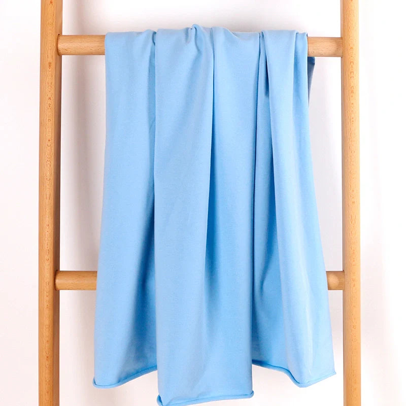 Un tissu en coton extensible French Terry de Longan Craft France, multicolore et confortable - parfait pour les vêtements de sport - est drapé sur une échelle en bois sur un fond blanc.