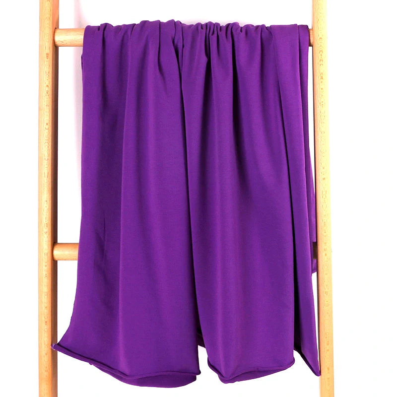 Un morceau de Tissu French Terry en coton extensible au mètre de Longan Craft France, confortable et multicolore, idéal pour les vêtements de sport, est drapé sur une échelle en bois sur fond blanc.