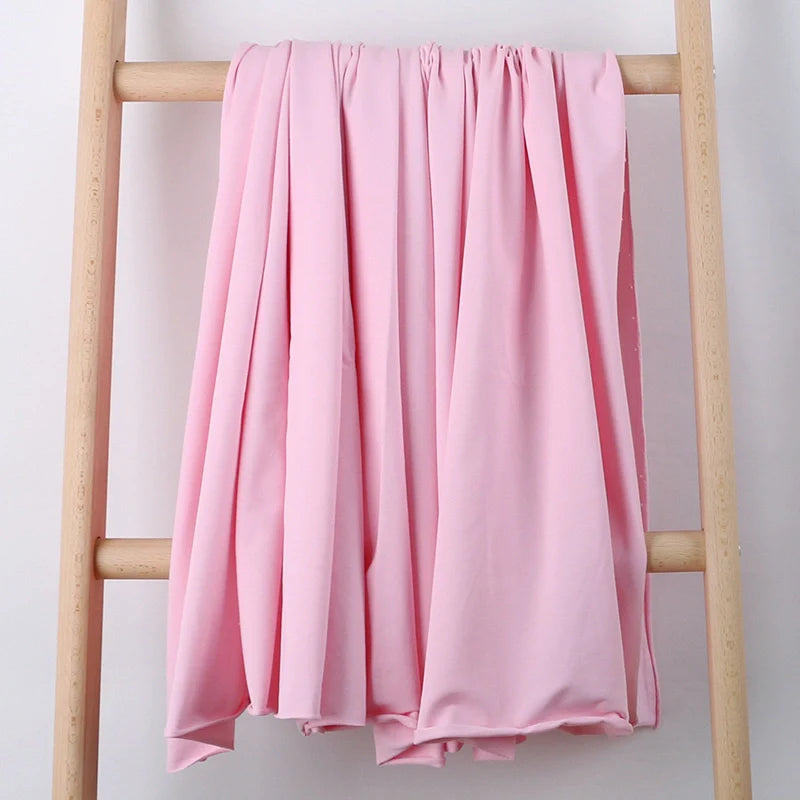 Un tissu stretch multicolore en coton French Terry de Longan Craft France drapé sur une échelle en bois clair contre un mur blanc uni, idéal pour les vêtements de sport et disponible au mètre.