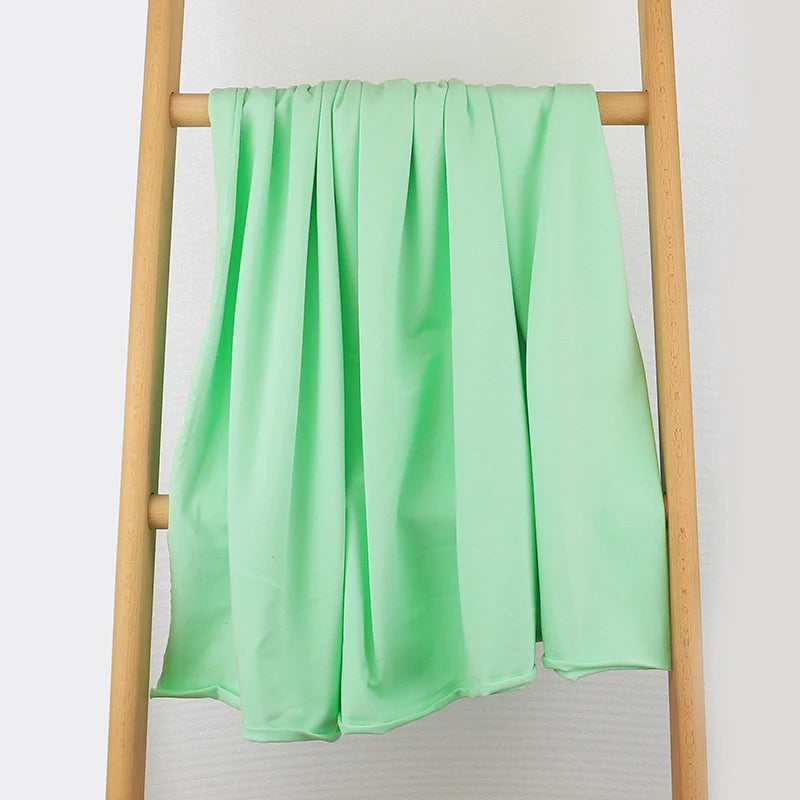 Un tissu multicolore en coton extensible de Longan Craft France est drapé sur le barreau central d'une échelle en bois, présenté sur un fond blanc uni, révélant sa texture confortable et ses plis doux.