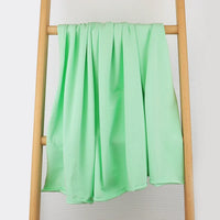 Un tissu multicolore en coton extensible de Longan Craft France est drapé sur le barreau central d'une échelle en bois, présenté sur un fond blanc uni, révélant sa texture confortable et ses plis doux.