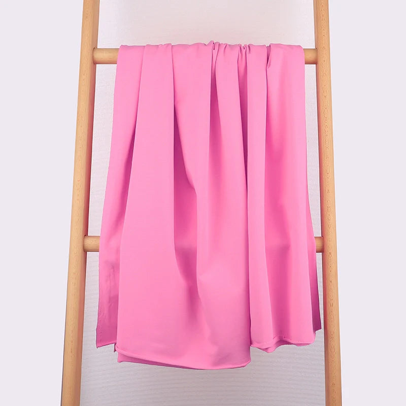 Un tissu multicolore en coton extensible French Terry de Longan Craft France est drapé sur une échelle en bois clair sur fond blanc, mettant en valeur sa texture lisse, idéale pour les vêtements de sport et les vêtements confortables.