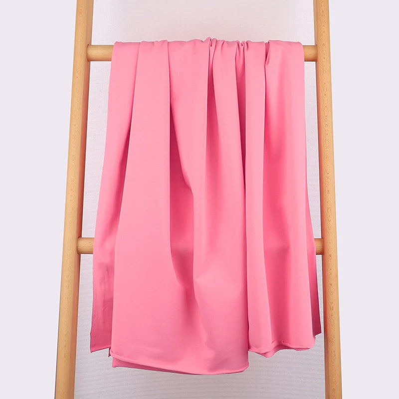 Une longueur de Tissu French Terry en coton extensible de Longan Craft France, idéal pour les vêtements de sport, est drapée sur une échelle en bois clair à trois barreaux sur un fond uni de couleur claire.