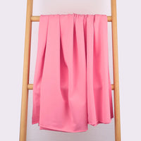 Une longueur de Tissu French Terry en coton extensible de Longan Craft France, idéal pour les vêtements de sport, est drapée sur une échelle en bois clair à trois barreaux sur un fond uni de couleur claire.