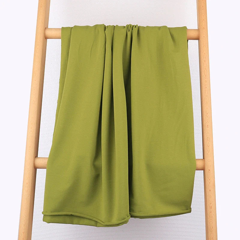 Un Tissu French Terry multicolore en coton extensible de Longan Craft France est exposé sur une échelle en bois clair contre un mur pâle - parfait pour des vêtements de sport confortables.