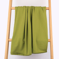 Un Tissu French Terry multicolore en coton extensible de Longan Craft France est exposé sur une échelle en bois clair contre un mur pâle - parfait pour des vêtements de sport confortables.