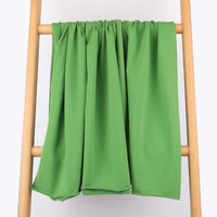 Un morceau de Tissu French Terry en coton extensible au mètre de Longan Craft France est drapé sur une échelle en bois sur un fond blanc, mettant en valeur sa texture lisse et confortable, idéale pour les vêtements de sport.