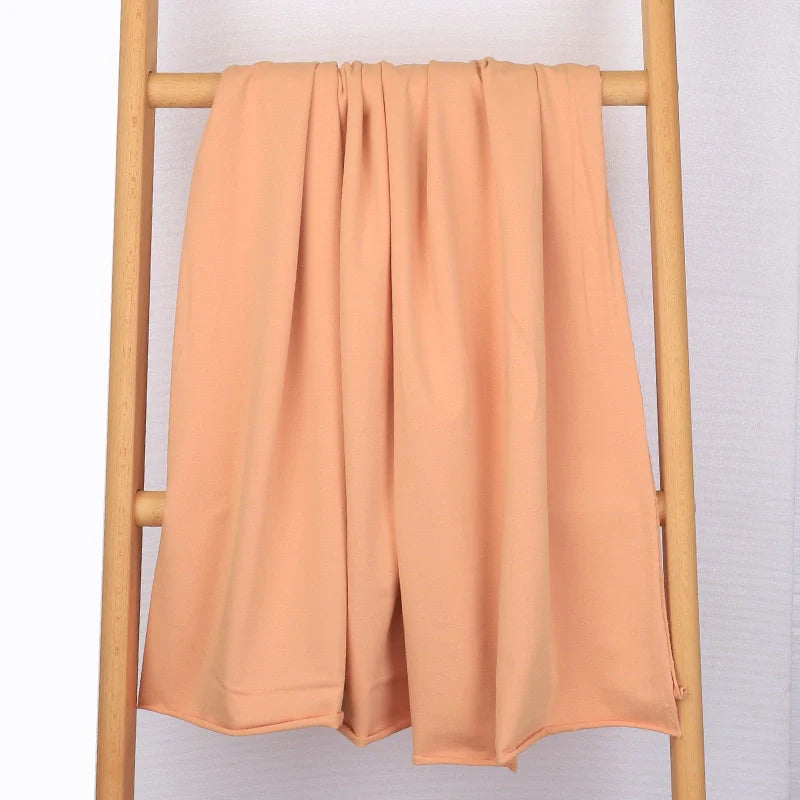 Un tissu multicolore en coton extensible French Terry de Longan Craft France est drapé sur une échelle en bois clair sur un fond blanc uni. Idéal pour les vêtements de sport, ce tricot confortable est vendu au mètre.