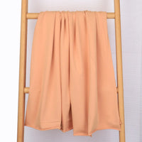 Un tissu multicolore en coton extensible French Terry de Longan Craft France est drapé sur une échelle en bois clair sur un fond blanc uni. Idéal pour les vêtements de sport, ce tricot confortable est vendu au mètre.