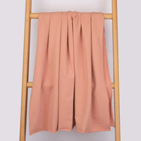 Un tissu de coton French Terry multicolore et extensible de Longan Craft France est drapé sur une échelle en bois contre un mur clair. Ce tissu confortable et tricoté est parfait pour les vêtements de sport et ajoute une touche douillette à la scène.