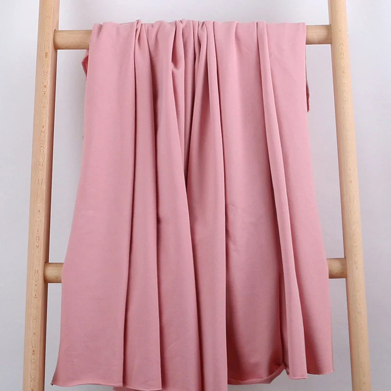 Le Tissu French Terry en coton extensible au mètre de Longan Craft France, confortable et idéal pour vêtements de sport, est drapé sur une échelle en bois clair devant un fond blanc, mettant en valeur ses plis souples et sa texture douce.