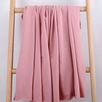 Le Tissu French Terry en coton extensible au mètre de Longan Craft France, confortable et idéal pour vêtements de sport, est drapé sur une échelle en bois clair devant un fond blanc, mettant en valeur ses plis souples et sa texture douce.