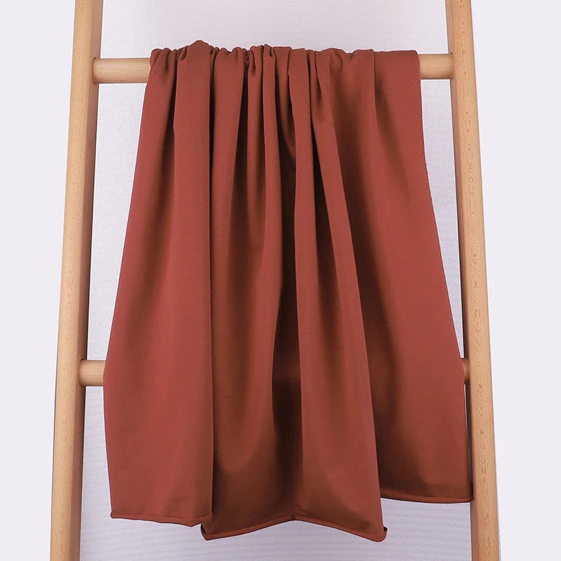 Le Tissu French Terry en coton extensible de Longan Craft France, confortable et multicolore, est présenté drapé sur une échelle en bois clair devant un fond blanc, idéal pour la confection de vêtements de sport.