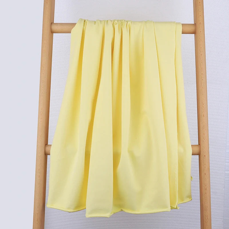 Le Tissu French Terry en coton extensible de Longan Craft France, idéal pour vêtements de sport, est présenté drapé sur une échelle en bois contre un mur clair, mettant en valeur sa texture douce et ses plis élégants.