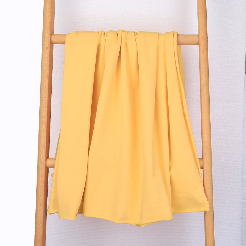 Le Tissu French Terry en coton extensible au mètre de Longan Craft France, un tricot multicolore confortable idéal pour les vêtements de sport, est drapé sur les barreaux d'une échelle en bois clair sur un fond blanc uni.