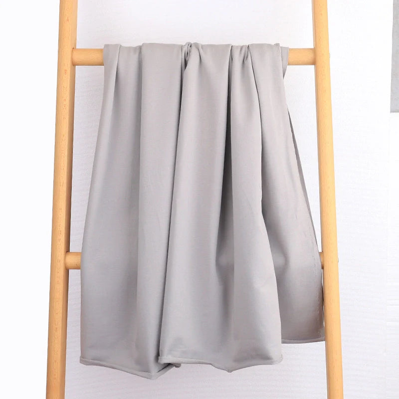 Le Tissu French Terry en coton extensible au mètre de Longan Craft France, un tissu tricoté multicolore confortable idéal pour vêtements de sport, repose sur les barreaux d'une échelle en bois clair devant un mur blanc texturé.