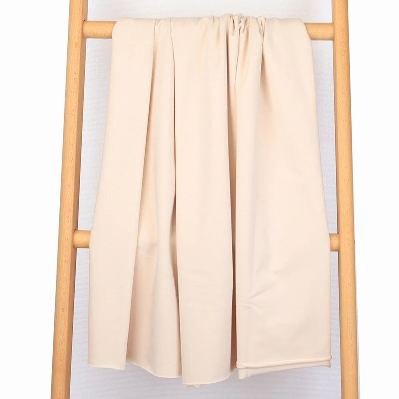 Le Tissu French Terry en coton extensible au mètre de Longan Craft France, confortable et parfait pour vêtements de sport, est drapé sur une échelle en bois devant un fond blanc, tombant librement et couvrant les barreaux centraux.