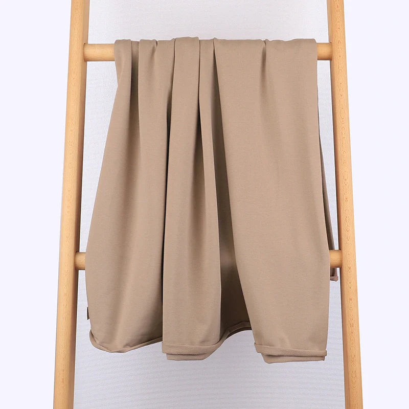 Un morceau de tissu multicolore en coton extensible French Terry de Longan Craft France est soigneusement suspendu à une échelle en bois clair sur un fond uni de couleur claire - confortable et idéal pour les vêtements de sport.