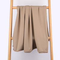 Un morceau de tissu multicolore en coton extensible French Terry de Longan Craft France est soigneusement suspendu à une échelle en bois clair sur un fond uni de couleur claire - confortable et idéal pour les vêtements de sport.