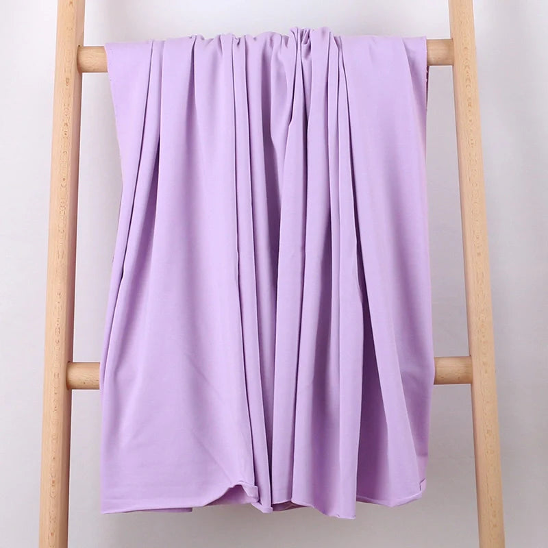 Une échelle en bois léger présente le Tissu French Terry en coton extensible au mètre de Longan Craft France, une maille multicolore confortable pour les vêtements de sport, drapée en plis souples sur un fond blanc uni.