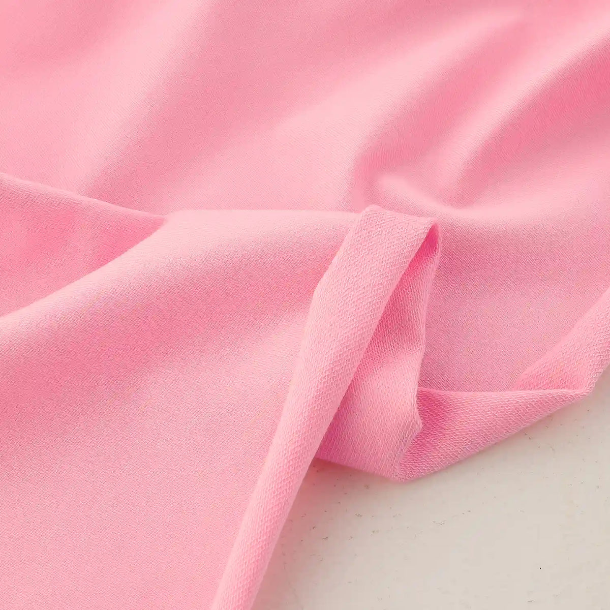 Gros plan sur le Tissu French Terry en coton extensible au mètre de Longan Craft France, rose pâle et lisse, drapé pour montrer les plis doux et la texture subtile - confortable et idéal pour les vêtements de sport.