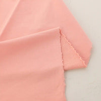 Un gros plan du Tissu French Terry en coton extensible au mètre de Longan Craft France montre un tissu rose clair aux bords non finis et légèrement effilochés, mettant en valeur sa texture douce et extensible, parfaite pour les vêtements de sport et les vêtements confortables.