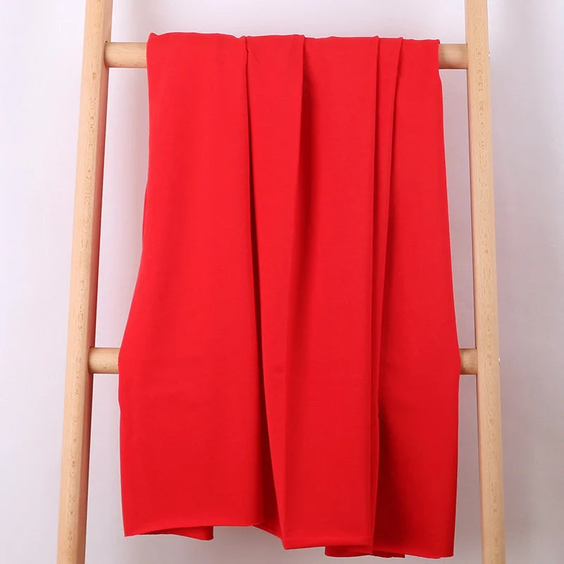 Le Tissu French Terry en coton extensible au mètre de Longan Craft France, un tissu tricoté multicolore idéal pour vêtements de sport, est posé sur les barreaux d'une échelle en bois clair sur fond blanc.