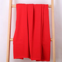 Le Tissu French Terry en coton extensible au mètre de Longan Craft France, un tissu tricoté multicolore idéal pour vêtements de sport, est posé sur les barreaux d'une échelle en bois clair sur fond blanc.