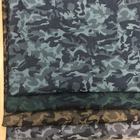 Trois pièces de Tissu denim jacquard camouflage extensible au mètre de Longon Craft France sont empilées, chacune en bleu-gris, vert et marron, affichant des motifs abstraits colorés dans un denim camouflage extensible pour vêtements.
