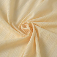 Le Tissu dobby jacquard ajouré rayé au mètre de Longan Craft France, un tissu en pur coton idéal pour l'habillement, est présenté en jaune clair avec un motif subtil de losanges et de rayures, tourbillonné à plat pour montrer sa texture douce et ses plis élégants.