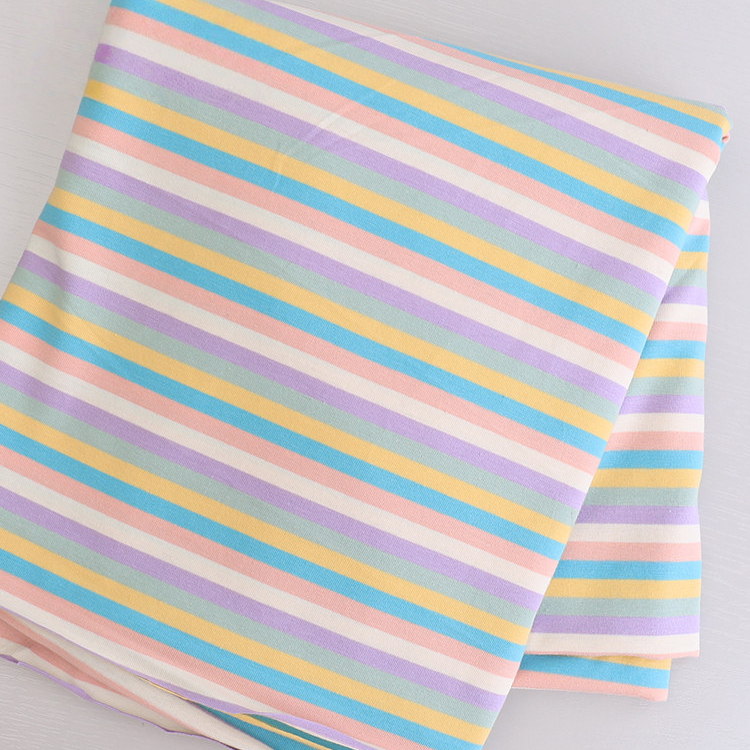 Tissu jersey rayé au mètre de Longan Craft France, en coton élasthanne extensible, présente des rayures pastel diagonales bleu, jaune, rose, violet et blanc-parfait pour confectionner des t-shirts manches courtes DIY.
