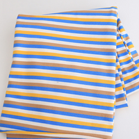 Un morceau de tissu jersey rayé au mètre - jersey coton élasthanne extensible avec des rayures bleues, jaunes, brunes et blanches - de Longan Craft France repose sur une surface blanche unie, idéale pour le bricolage de t-shirts à manches courtes.