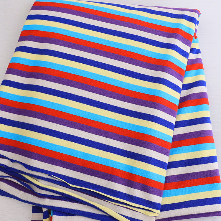Un morceau plié de Longan Craft France Tissu jersey rayé au mètre en jersey de coton-elasthane extensible confortable, avec des rayures diagonales violettes, rouges, jaunes, bleues et blanches, parfaites pour les t-shirts à manches courtes DIY.