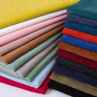 Une pile bien empilée de Longan Craft France Tissu velours côtelé épais 8 côtes au mètre, en jaune, rose, marron, gris, bleu, rouge, vert et noir, ajoute une touche élégante à la décoration intérieure grâce à sa texture douce et à son motif de rangées horizontales.