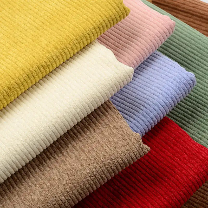 Des pièces vibrantes de Tissu velours côtelé épais 8 côtes au mètre de Longan Craft France en jaune, rose, vert, marron, crème, bleu et rouge sont empilées en diagonale - idéal pour ajouter une texture douillette à votre ameublement.