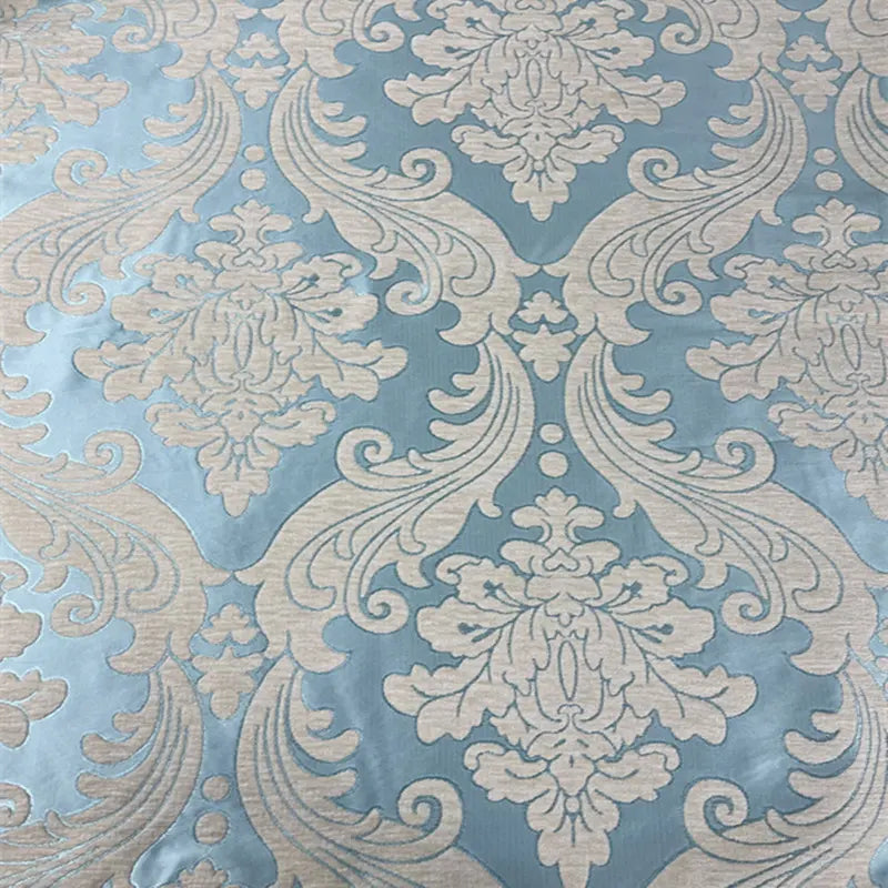 Gros plan sur le Tissu chenille damassé épais au mètre de Longan Craft France, qui présente un motif floral et de volutes beige vintage sur fond bleu clair - un tissu jacquard idéal pour une décoration intérieure raffinée ou des projets de tapisserie d'ameublement.