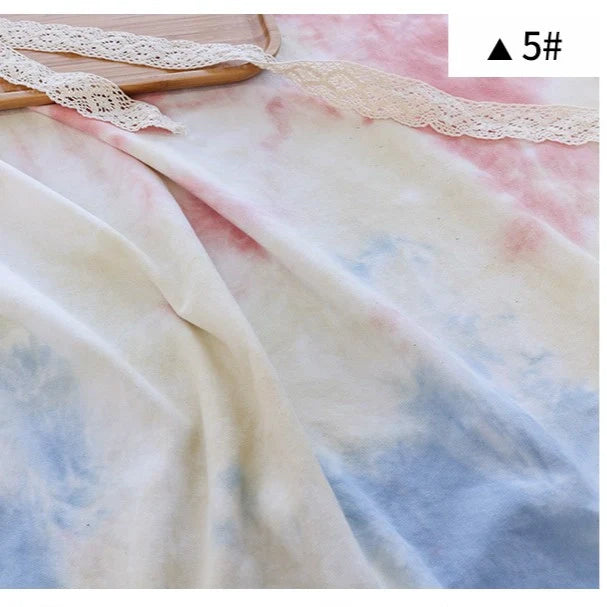Un morceau de tissu de coton French Terry de Longan Craft France en tie-dye rose pastel, bleu et crème avec une bande de dentelle blanche près du haut, étiqueté "▲5#". Parfait pour des vêtements confortables (Tissu French Terry imprimé en dégradé).