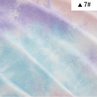 Un gros plan du Tissu French Terry en coton tie-dye au mètre de Longan Craft France montre des tons pastel doux de violet, de bleu et de rose pâle. Une boîte blanche avec un triangle noir et "7#" apparaît dans le coin supérieur droit.