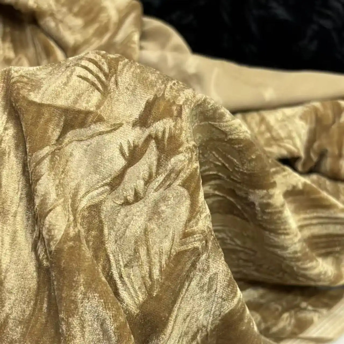 Un gros plan du tissu velours damassé au mètre de Longan Craft France montre son motif jacquard classique en or et beige, élégamment drapé avec des plis et des ombres pour un aspect doux et luxueux, idéal pour la confection de vêtements.