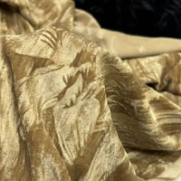 Un gros plan du tissu velours damassé au mètre de Longan Craft France montre son motif jacquard classique en or et beige, élégamment drapé avec des plis et des ombres pour un aspect doux et luxueux, idéal pour la confection de vêtements.