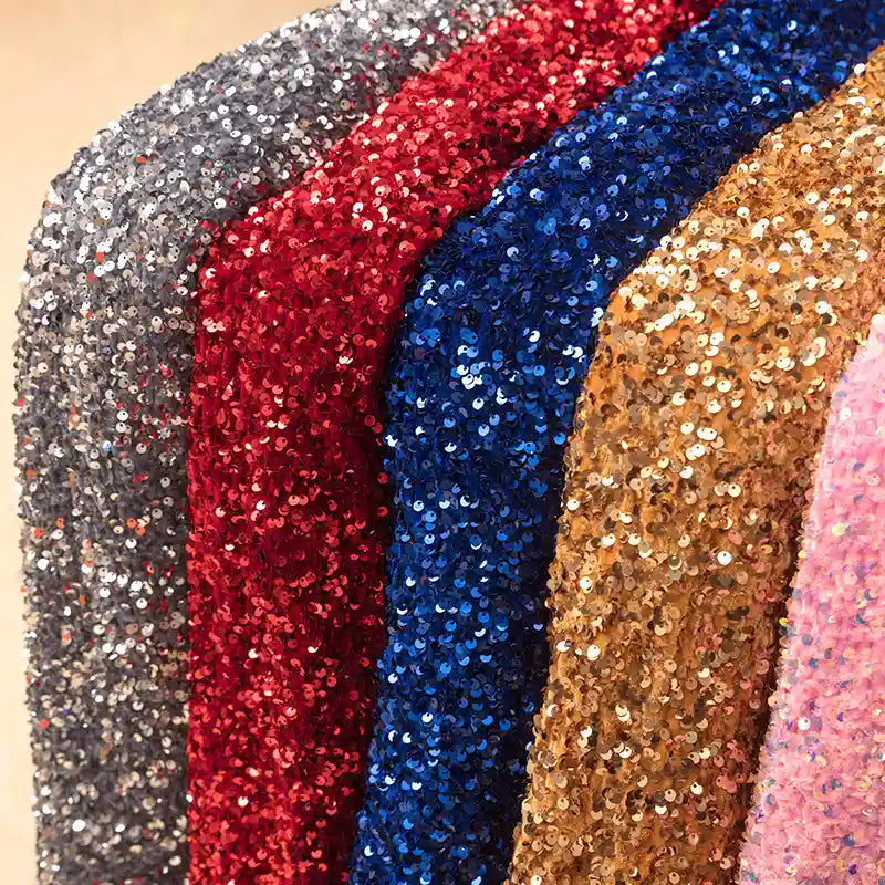 Gros plan sur le Tissu en velours extensible à paillettes de Longan Craft France, présenté en argent, rouge, bleu, or et rose. Le tissu extensible à paillettes reflète la lumière pour un effet scintillant, idéal pour la scène et les tenues de mode.