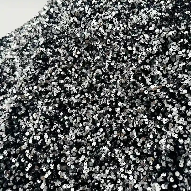Un gros plan du tissu en velours extensible à paillettes de Longan Craft France montre des paillettes argentées et noires densément emballées sur un tissu extensible, créant un aspect brillant et texturé, idéal pour les costumes de scène et la mode.