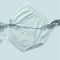 Un tissu pointelle côtelé polyester vert clair de Longan Craft France, vendu au mètre pour les vêtements d'intérieur DIY, est partiellement immergé dans l'eau sur un fond bleu clair uni, avec des éclaboussures et des bulles d'air visibles autour du tissu.