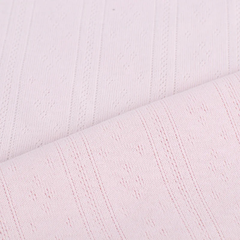 Gros plan sur le tissu Longan Craft France pointelle côtelé vertical au mètre en rose clair, présentant un motif texturé subtil avec de fines lignes en relief - un tissu polyester parfait pour les vêtements d'intérieur DIY.